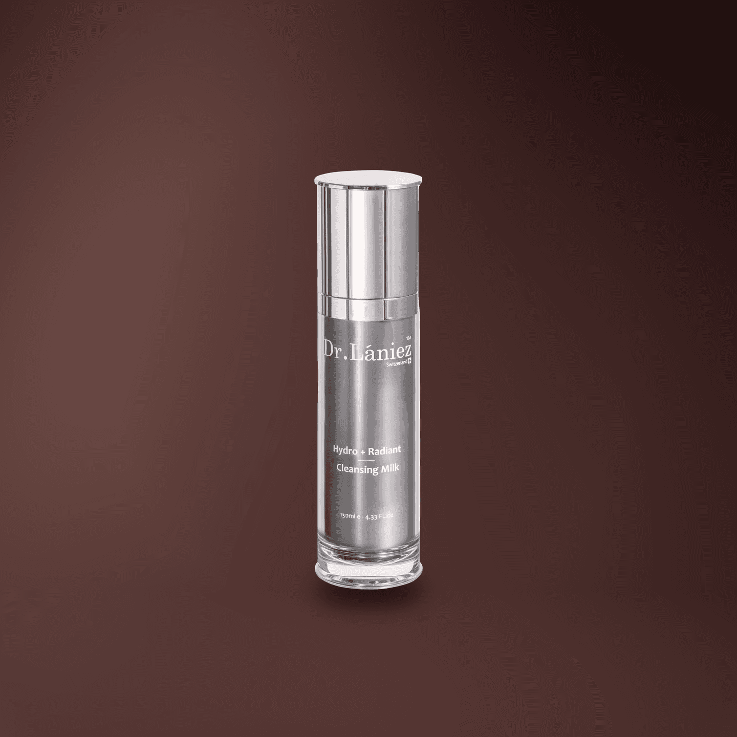 Silver pump bottle of Hydro + Radiant Cleansing Milk, 130 ml, lit on a warm plum studio backdrop.